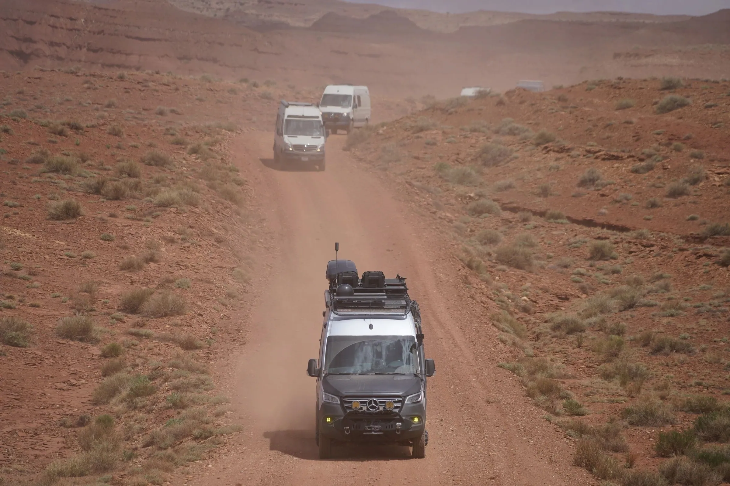 Camper vans raising dust on a red dirt road